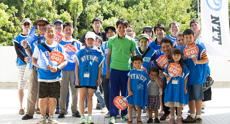 Image: Group photograph of Tadashi Horikoshi surrounded by volunteer athlete reporters and Kids' Reporters. Everyone is smiling at the camera.