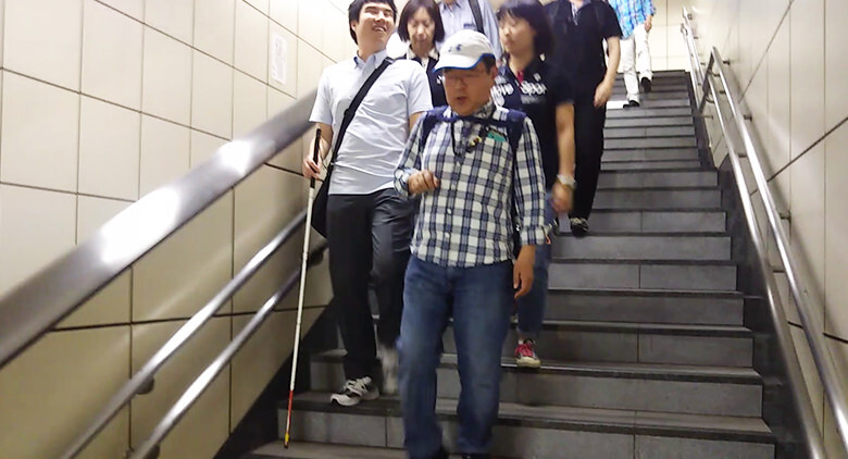 Image: Photograph of the survey group descending stairs at the station nearest the sporting venue. The photograph also shows a visually impaired person carrying a white cane.