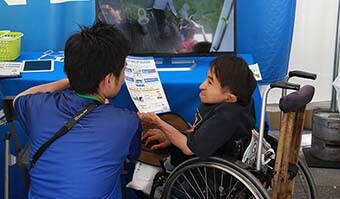 Image: Photograph from behind of NTT staff asking visually/physically impaired volunteers for their opinions regarding barrier-free facilities.