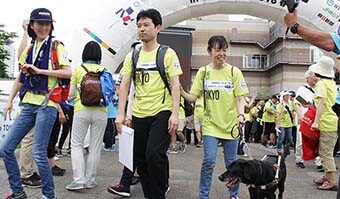 Image: Photograph of a scene from the Japan Walk venue. A girl and man with a guide dog for the blind are smiling as they walk along.