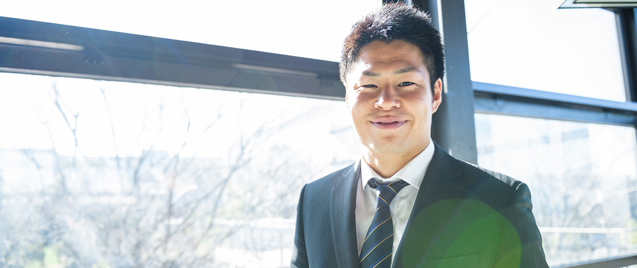 Image: Photograph of a smiling Kazushi Hano dressed in a suit.