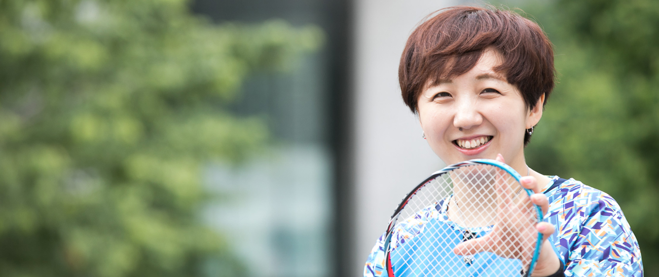 Image: Ms. YAMAZAKI smiling happiily as she holds a badminton racquet