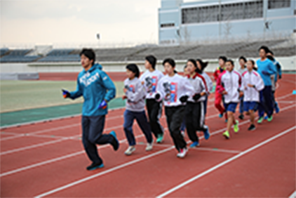 写真：NTT西日本陸上競技部によるふれあい陸上教室で、競技場のトラックをランニングする選手と子どもたちの様子