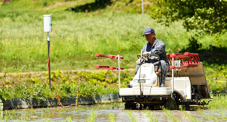 画像：ドコモのICTセンサーで管理された水田にトラクターを走らせる阿部さんの写真。