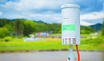 Image: Photograph of DOCOMO's paddy sensors against the background of the sprawling rural landscape of Minamisanriku Town.